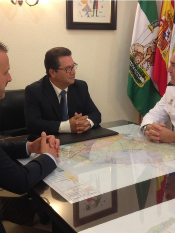 Reunión entre un oficial de marina y un representante en un escritorio con mapas y banderas.