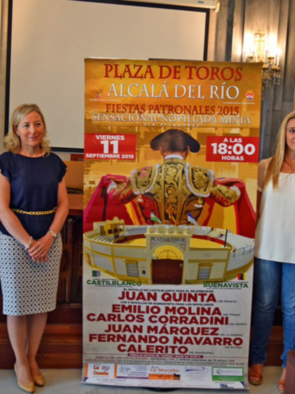 Personas posando frente a un cartel informativo sobre las Fiestas Patronales de Alcalá del Río 2015.