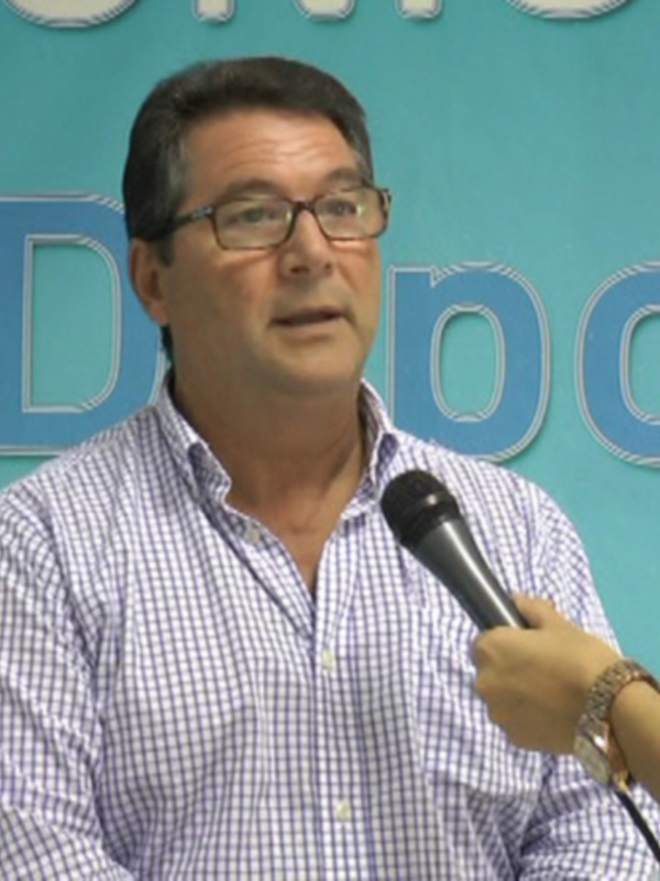 Hombre hablando en un evento con un fondo azul y letras blancas.
