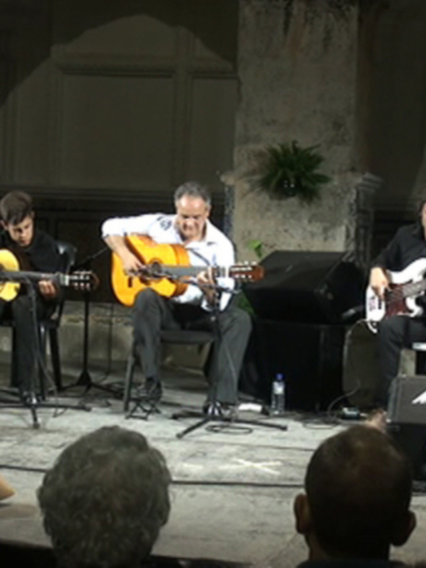 Concierto de música clásica en un escenario acústico con músicos tocando guitarra, piano y batería.