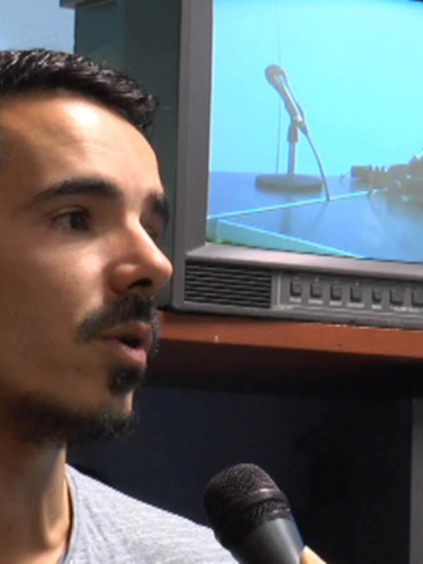 Entrevista en un estudio de radio con microfonos y monitores de televisión en el fondo.
