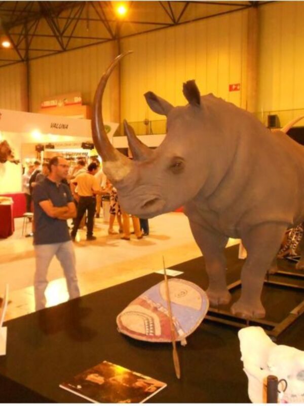 Exposición de modelos de animales en una feria. En primer plano, un rinoceronte blanco y un leopardo. En el fondo, visitantes observan las exposiciones.