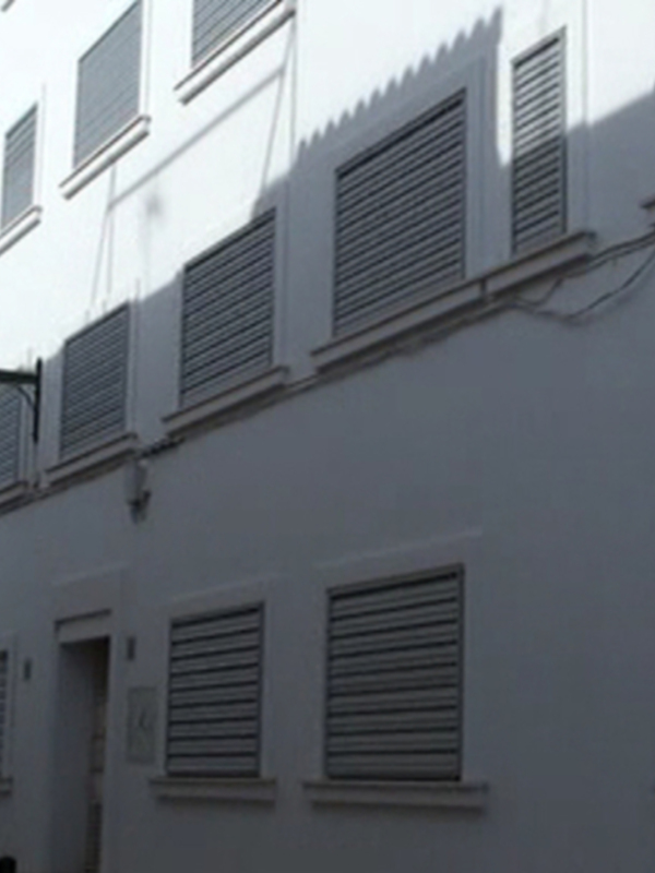 Fachada de edificio blanco con ventanas de persianas en una calle tranquila.