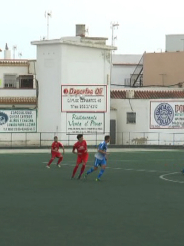 Juego de fútbol en un campo con publicidad en el muro y edificios al fondo.