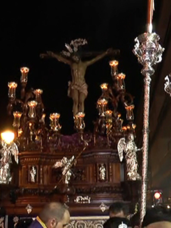Procesión religiosa nocturna con estandartes y crucifijo, iluminado por candelabros y velas.
