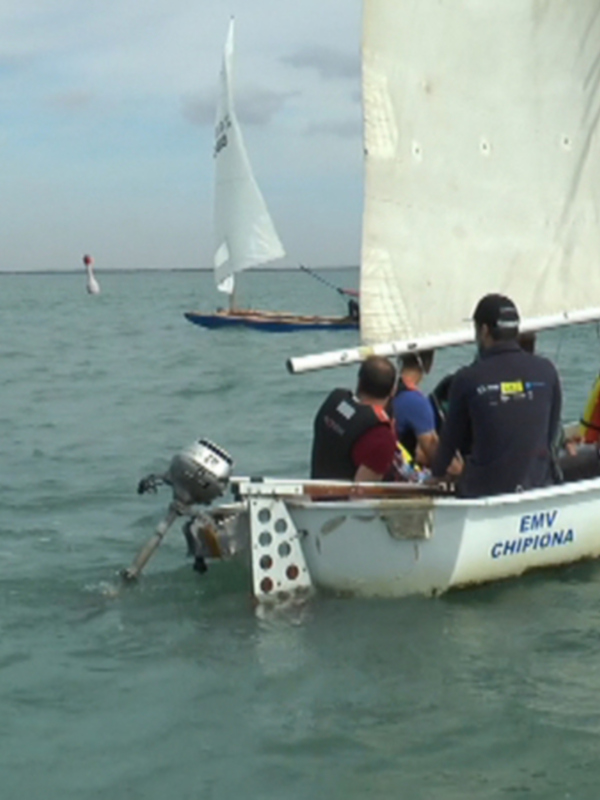 Un grupo de personas navega en un barco de vela en el mar, con otras embarcaciones en el horizonte.