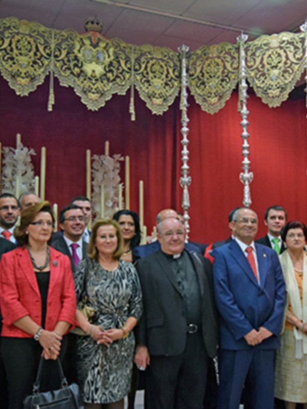 Grupo de personas en trajes formales posando en un evento formal con telón rojo y decoración dorada.