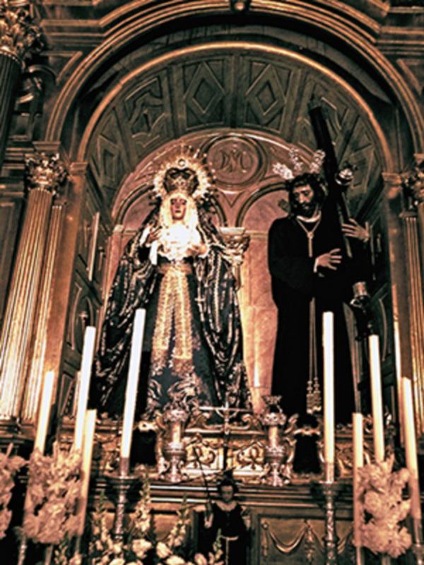 Altar en iglesia con imágenes religiosas y velas encendidas.