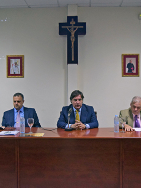 Reunión en un ambiente formal con un crucifijo y imágenes religiosas en el fondo.
