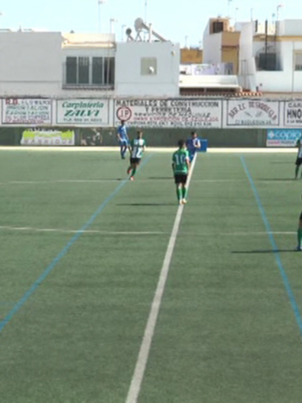 Partido de fútbol en un campo con publicidad alrededor y edificios en el fondo.