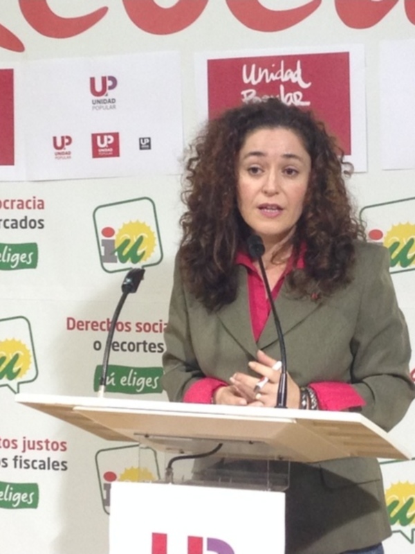 Mujer hablando en un evento político con carteles de Unidad Popular en el fondo.