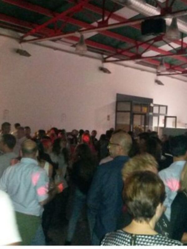Fotografía de una multitud en un evento, con personas de diferentes edades y estilos de vestir, en un entorno con iluminación artificial y estructuras de metal en el techo.