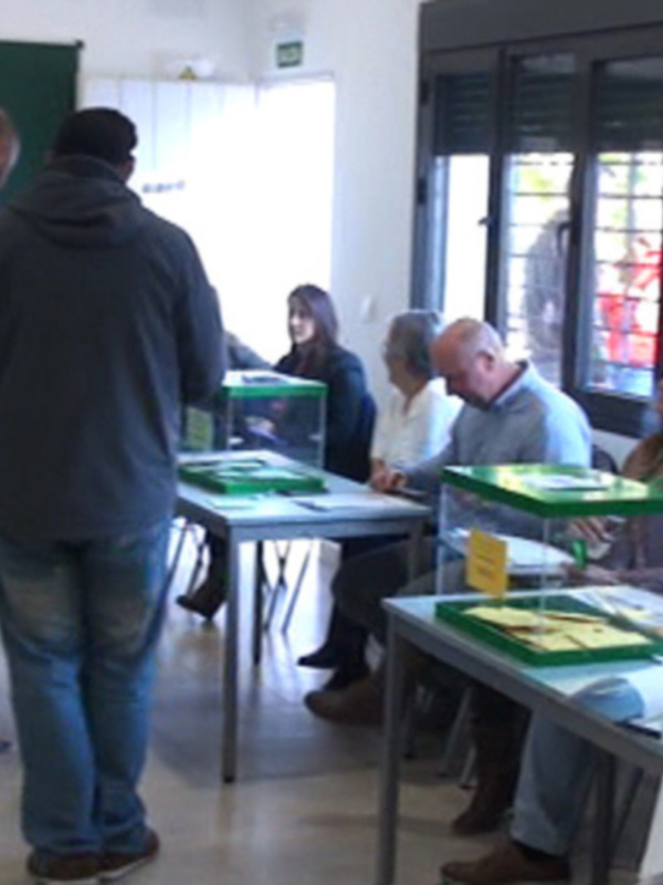Votación en una mesa electoral con personas esperando y votando.