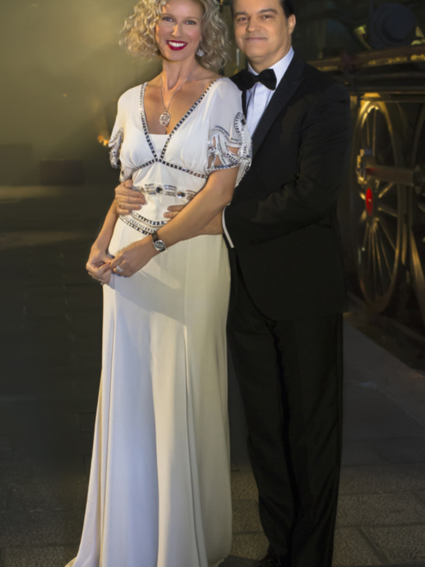 Una pareja elegante en traje y vestido blanco posa juntos en un entorno nocturno iluminado.