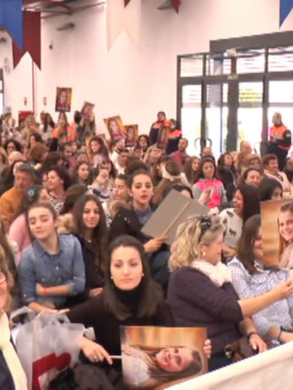 Una multitud de personas en un evento, algunas sosteniendo fotos de personas famosas.