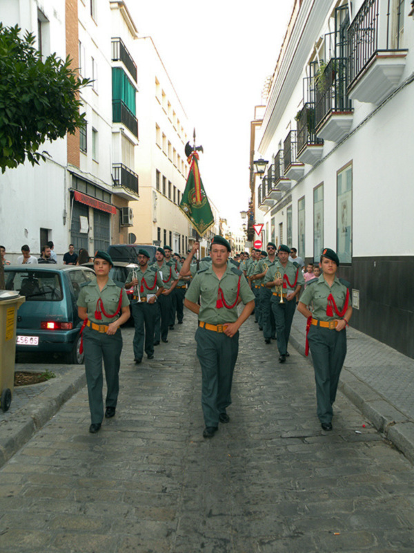 Desfile militar con bandera y trompetas en una calle urbana.