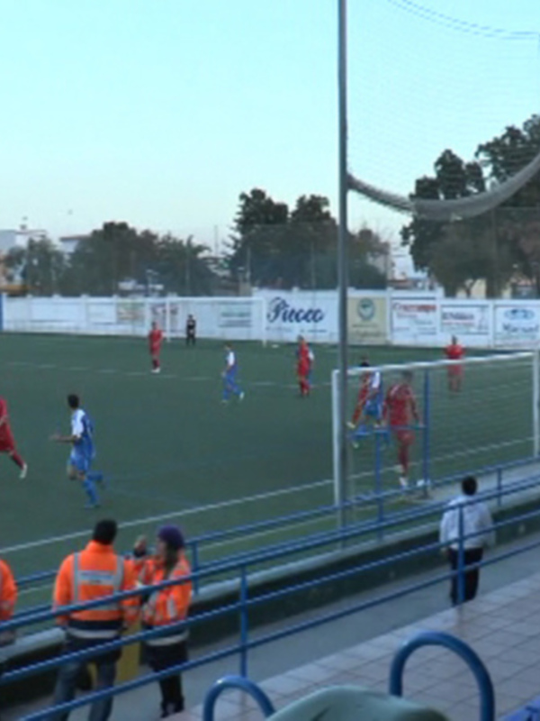 Juego de fútbol en un estadio local con aficionados observando desde las gradas.