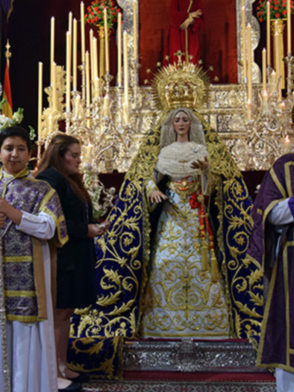 Procesión religiosa con imágenes santas y niños vestidos de sacerdotes en un interior ornado.