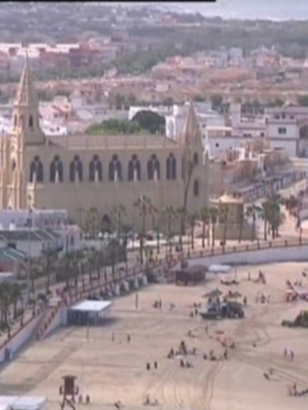 Vista aérea de una ciudad costera con una catedral gótica y una playa con gente disfrutando del sol.