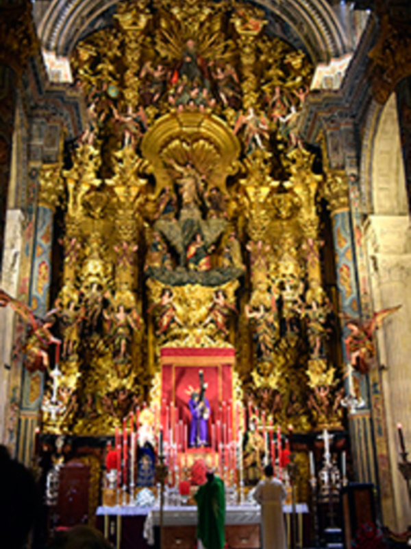 Interior de una iglesia con altar ornado y altares laterales dorados, con figuras religiosas y candelabros en el centro.