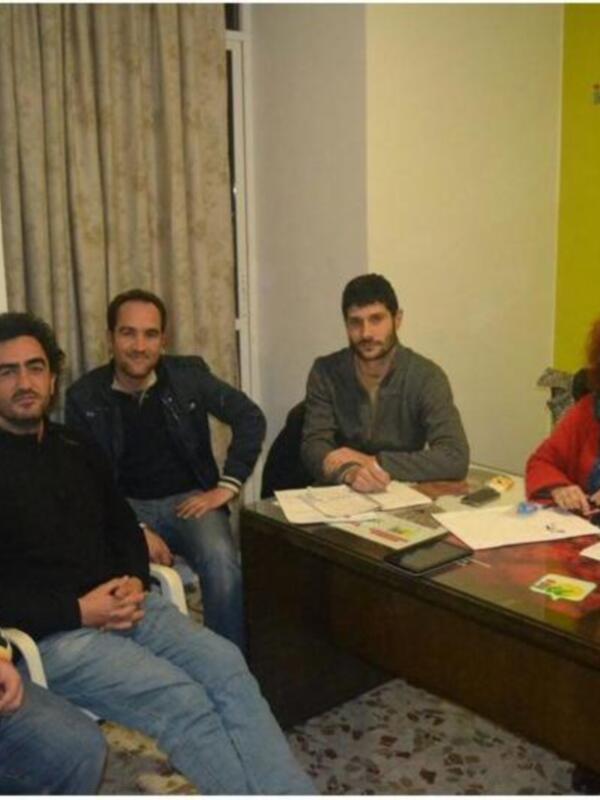 Un grupo de personas sentadas en una sala, con un hombre en el centro sonriendo y sosteniendo una tableta digital, mientras otros dos hombres y una mujer observan.