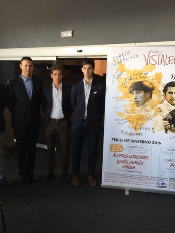 Cuatro hombres en trajes posan junto a un cartel informativo sobre la Feria de Invierno 2016 en Vistalegre, con detalles sobre los toreros Álvaro Lorenzo, Ginés Lorenzo, Marín y Varela, y la corrida de toros de David Mora Fortes.