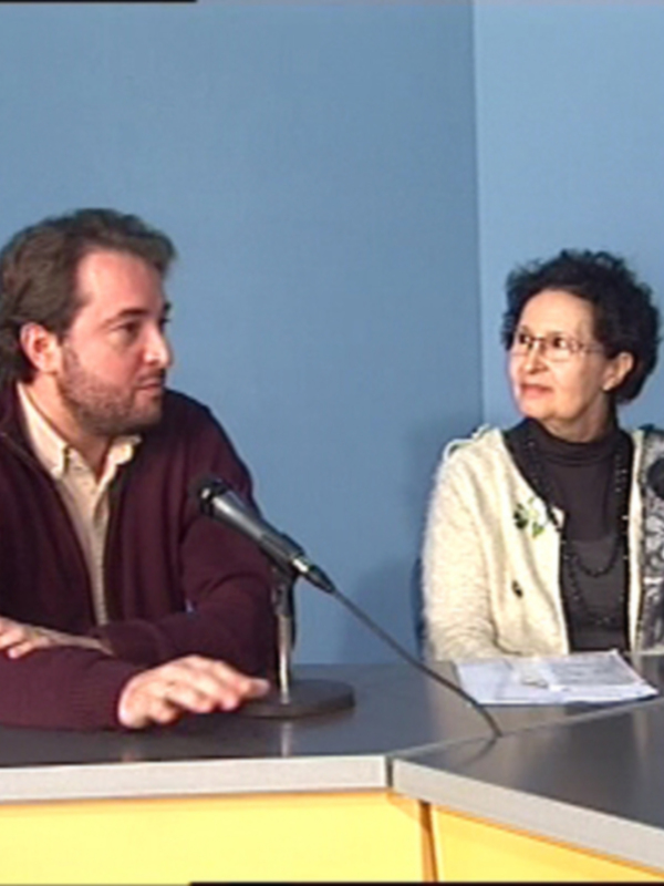 Entrevista en estudio radiofónico con dos personas sentadas frente a micros, conversando.