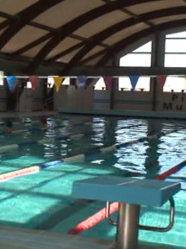 Interior view of a municipal swimming pool with swimmers practicing in lanes.