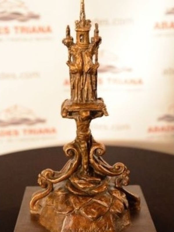 Un candelabro de bronce con una figura en la parte superior, posiblemente una estatua de un personaje histórico o religioso, sobre un pedestal con detalles ornamentales.