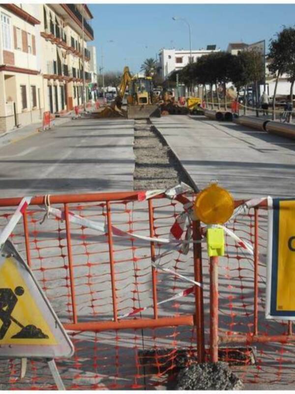 Calle cortada por obras en una ciudad costera, con obras de construcción y señalización de seguridad.