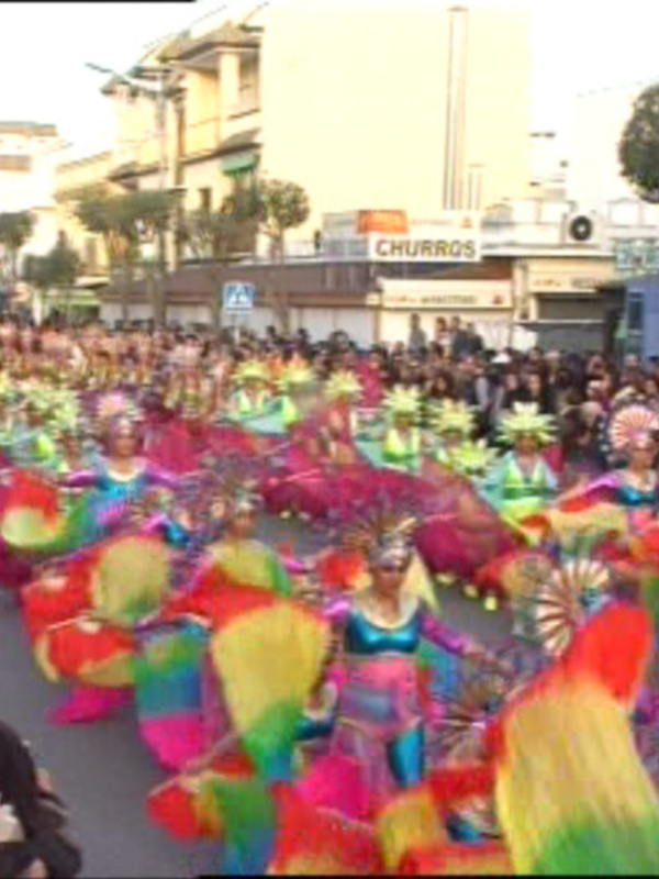 Desfile de disfraces coloridos en una calle con espectadores observando el evento festivo.