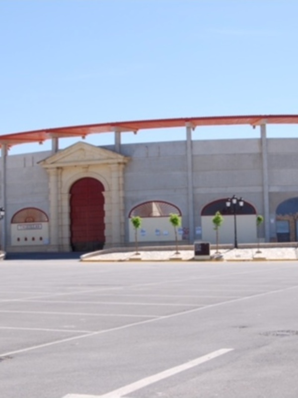 Plaza de toros vacía con edificio de color rojo y blanco bajo un cielo azul claro.