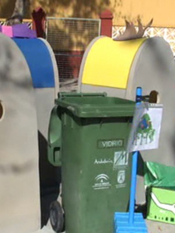 Niños jugando con contenedores de reciclaje en un patio escolar.