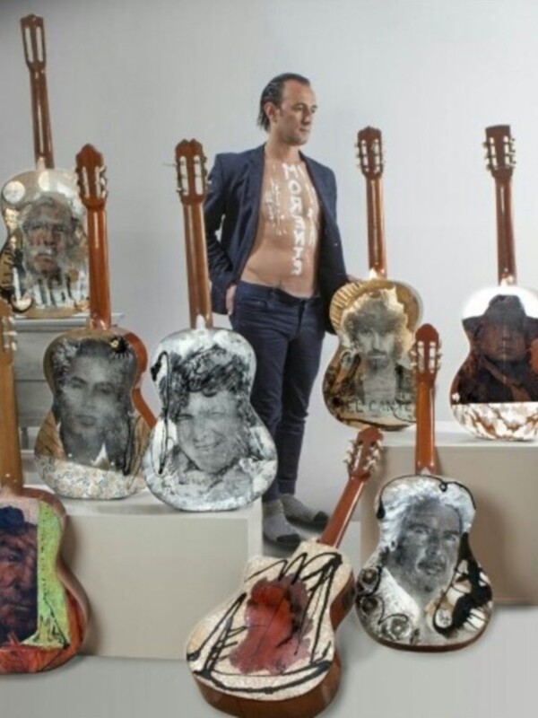 Un artista posa junto a una colección única de guitarras, cada una con un retrato de un famoso músico. La creatividad y el arte se combinan para crear una obra única y memorable.