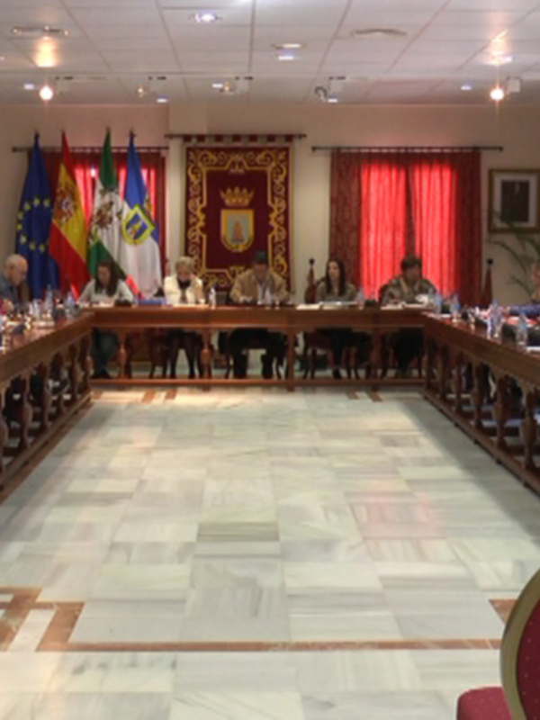 Sala de reuniones con una larga mesa alineada con sillas rojas y banderas en el fondo.