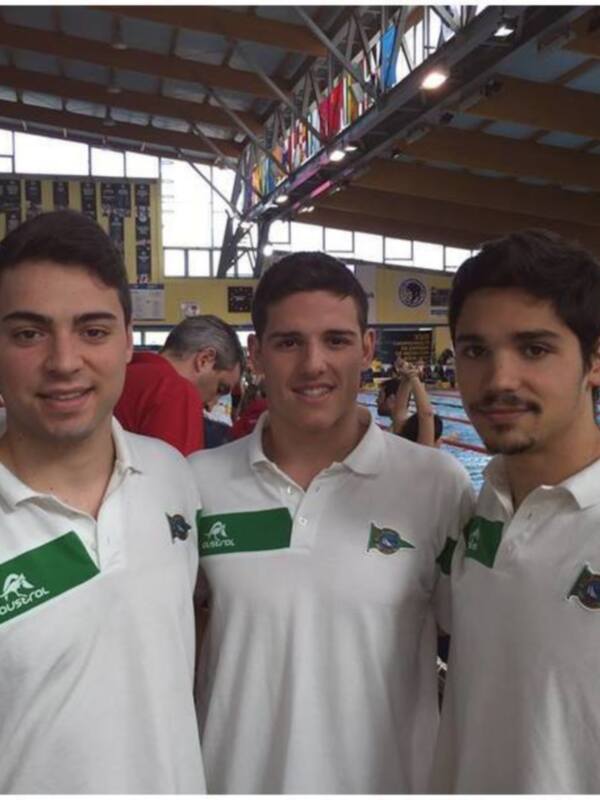 Tres nadadores posando en una piscina olímpica, con vestimentas deportivas y logos de sponsors visibles.