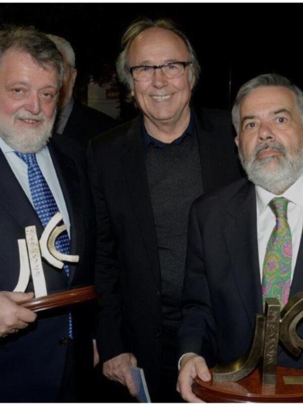 Tres hombres en trajes posando con trofeos en un evento de gourmet.