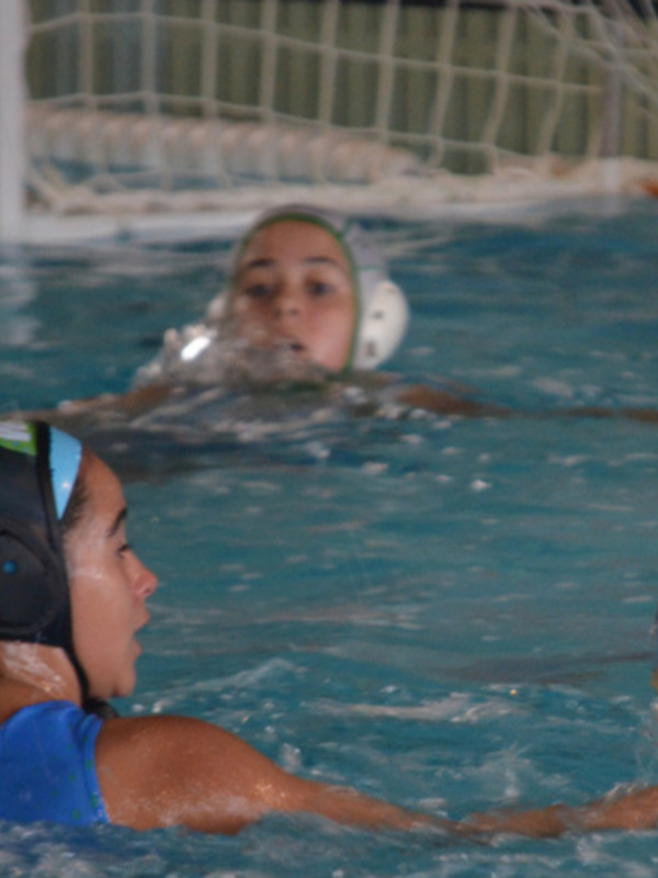 Jugadoras de waterpolo en acción durante un partido en una piscina cubierta.