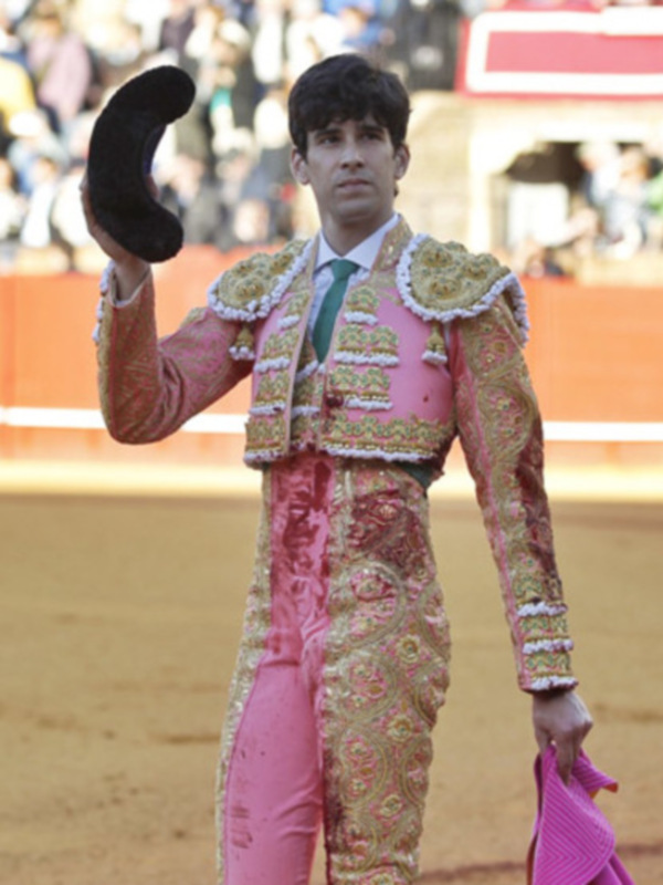 Joven matador en traje de luces saludando con el sombrero en un ruedo de toros.