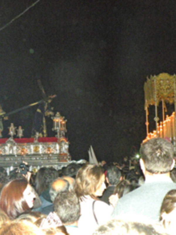 Procesión nocturna con estandartes y figuras religiosas, rodeada de fieles observadores.