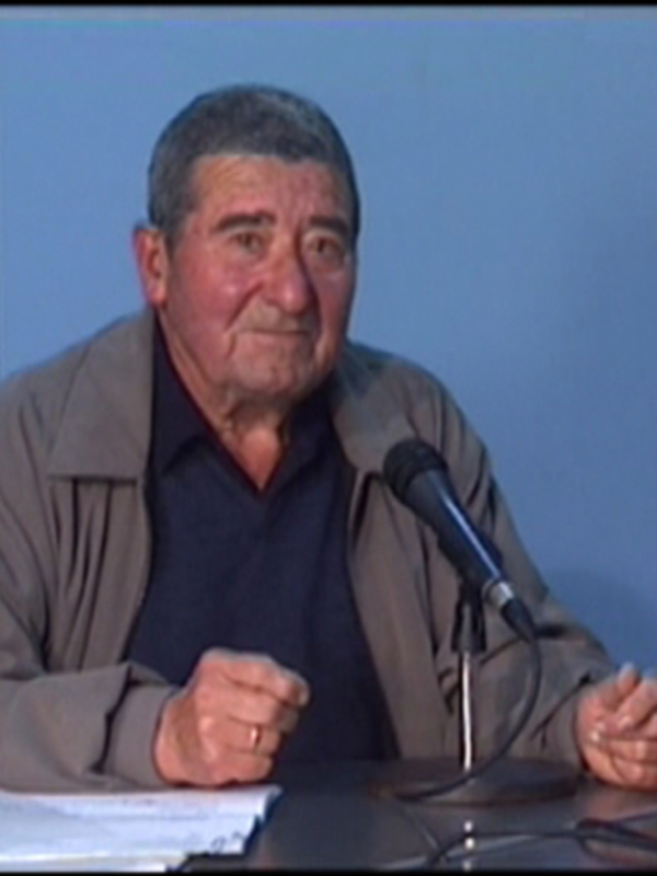 Hombre sentado en una mesa con un micrófono, posiblemente en una conferencia o entrevista.