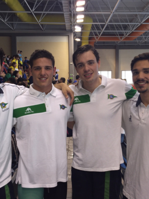 Equipo de natación posando en el borde de una piscina, con uniformes blancos y verde, sonriendo para la cámara.