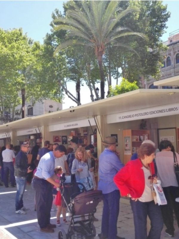 Pozo de una feria de libros en una plaza con palmeras y edificios históricos en el fondo.