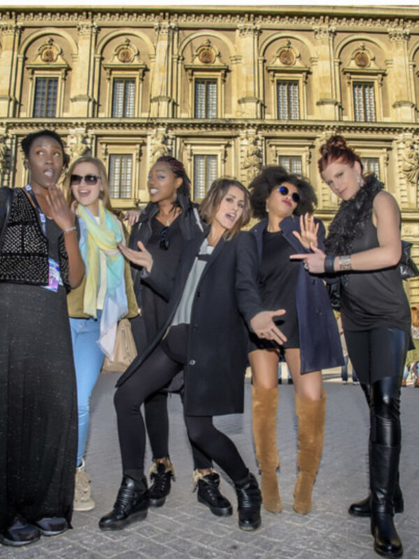 Cinco mujeres posan juntas en un patio de piedra frente a un edificio histórico con arcos y ventanas alineadas.