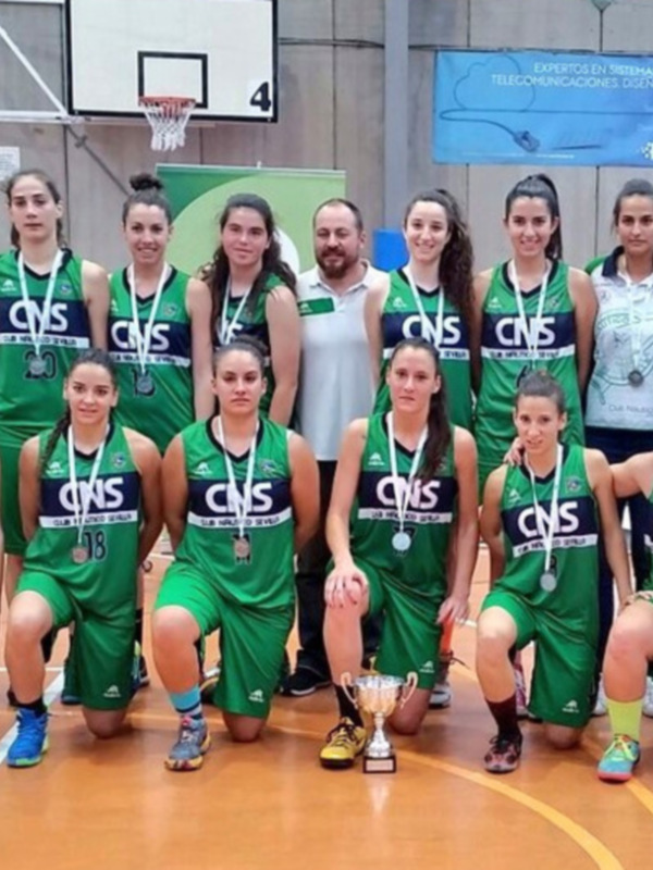 Equipo femenino de baloncesto posando con sus medallas y el trofeo ganado en un partido de competición.