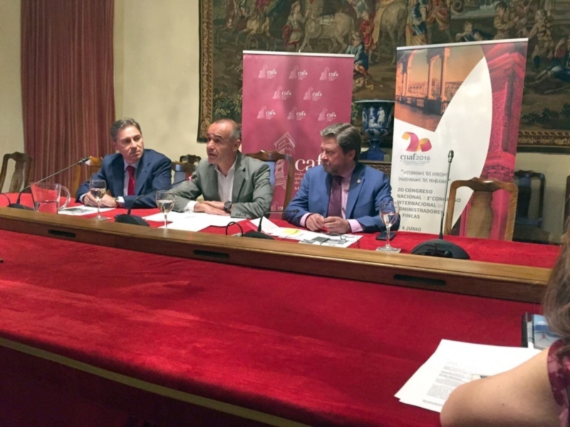 Tres hombres sentados en una mesa con pancartas de conferencia en el fondo.