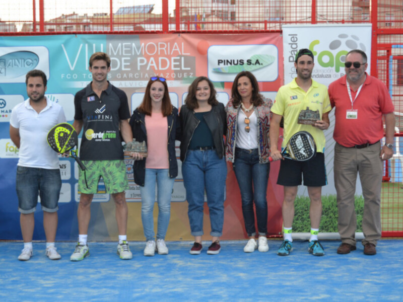 Equipo de padel posando en un torneo de pádel, con un banner de patrocinio en el fondo.