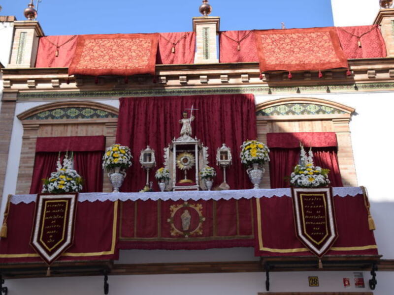 Altar con estandarte rojo y flores, representando una celebración religiosa.
