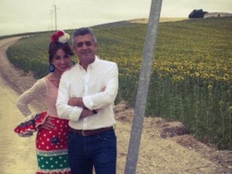 Un par de personas posando en un camino rural con campos de girasoles al fondo.
