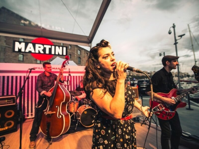 Banda tocando en vivo en un escenario al aire libre con el logo de Martini en el fondo.